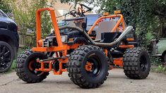 an orange four wheel drive vehicle parked next to a green car in a driveway area