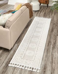 a living room with wood flooring and white rugs on the floor, next to a beige couch