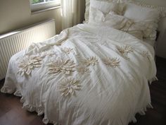 an unmade bed with white linens and flowers on the comforter, next to a radiator