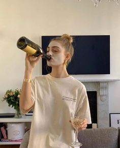 a woman drinking from a wine glass while standing in front of a fireplace