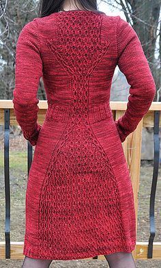 a woman in a red knitted dress standing on a deck with her back to the camera