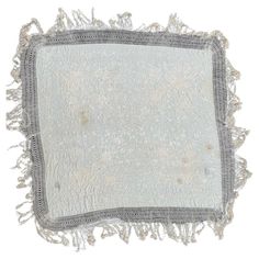 a white and grey pillow with fringes on the edges, in front of a white background