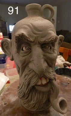 a clay sculpture of an old man's head with a pipe in his mouth