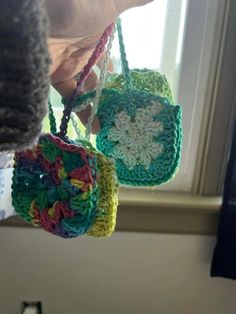 two crocheted purses hanging from a window sill in someone's hand