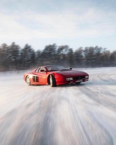 a red sports car driving down a snow covered road with trees in the back ground