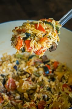 a spoon full of rice and vegetables being lifted from a skillet with a fork