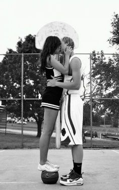 two people standing on a basketball court with an umbrella over their heads and one person kissing the other