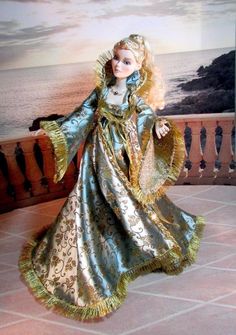 a doll is dressed in an ornate blue and gold dress, standing on a balcony overlooking the ocean