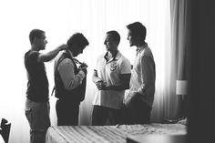 a group of men standing next to each other in front of a bed and window