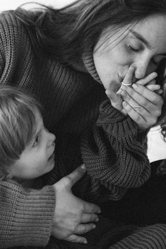 a woman and child sitting on the floor with their hands together, one is holding something in her mouth