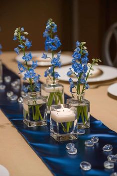 blue flowers are in vases on a table with water and glass candlesticks