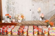 many jars of food are lined up on a table next to flowers and vases