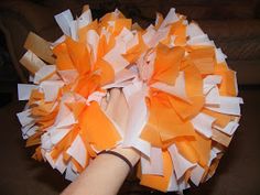 a hand holding a large orange and white pom - pom