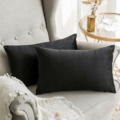 two black pillows sitting on top of a gray couch next to a white blanket and table