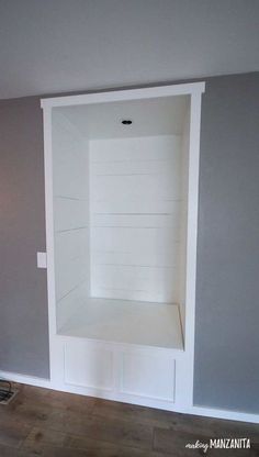 an empty shelf in the corner of a room with gray walls and wood flooring