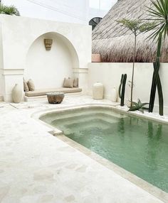 a small pool in the middle of a patio with a thatched roof above it