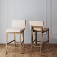 two wooden stools with white upholstered leather seats in front of a wall