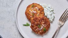 two fried chicken patties on a white plate with blue cheese sauce and a fork