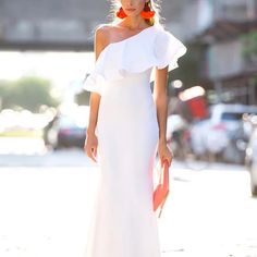 a woman in a white dress is walking down the street with an orange purse on her shoulder