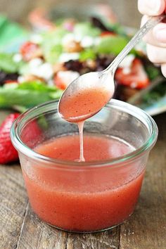 a spoon full of dressing being held over a bowl with salad on the table in the background