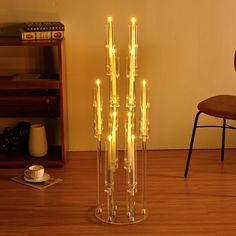 a tall glass vase filled with candles sitting on top of a wooden floor next to a chair