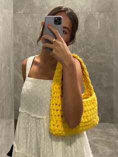 a woman taking a selfie in front of a mirror wearing a yellow crochet bag