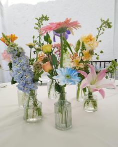 three glass vases filled with colorful flowers on top of a white tablecloth covered table