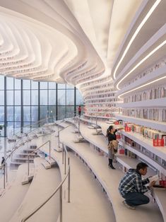 two people are sitting on the floor in a large room with many bookshelves