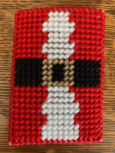 a red and white knitted square with a gold buckle on the center, sitting on a wooden surface