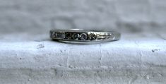 This Art Deco Vintage Diamond Channel Wedding Band is a classic - and would make a great wedding band or stackable today. Crafted in 18K White Gold, the band features 7 Single Cut Diamonds, approximately 0.21ct in weight, of excellent H/VS1 quality, all Channel Set, with a lovely Art Deco Floral Shoulders, and engraving. Beautiful and sparkly! Other Important Details: The band is a Size 4.75. The band is stamped '18K', and has been tested to be 18K White Gold. The band weighs 1.9 grams. The band Classic Bands With Single Cut Diamonds For Promise Ring, Classic Stackable Cubic Zirconia Bands, Formal Stackable Diamond Bands, Timeless Stackable Wedding Bands, Formal Stackable Cubic Zirconia Bands, Formal Stackable Bands With Cubic Zirconia, Classic Silver Bands With Single Cut Diamonds, Classic Stackable Half Eternity Rings For Anniversary, Classic Stackable Eternity Band For Promise