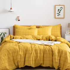 a bed with yellow comforter and pillows in a white room next to a plant