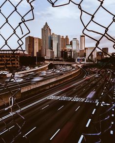 the city skyline is seen through a chain link fence with cars driving on the road