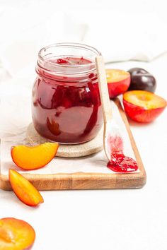 a glass jar filled with fruit jam next to sliced peaches