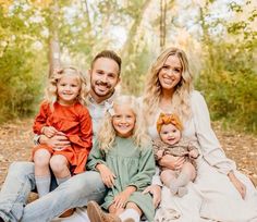 a man and woman with two children sitting on a blanket in front of some trees