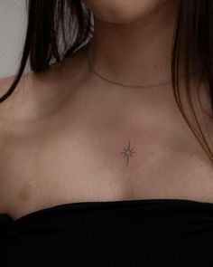 a close up of a woman's chest with a small cross tattoo on it