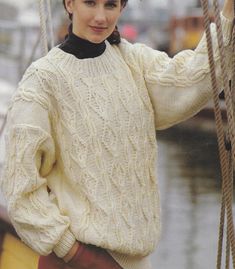 a woman standing next to a boat wearing a white sweater and red pants with black collar