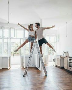 a man and woman standing on top of a steplader in an open room