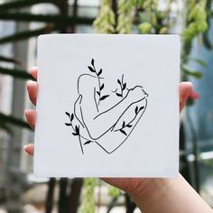 a hand holding up a paper with a drawing of a heart and leaves on it