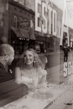 a man and woman sitting at a table in front of a store window, talking