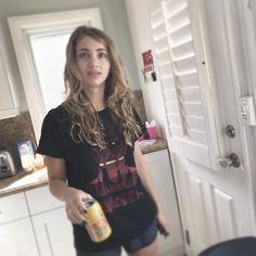 a woman standing in a kitchen with a can of beer next to her and looking at the camera