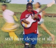 there is a young boy that is playing the guitar in front of other kids on the train tracks