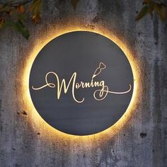 a round sign with the word morning written in cursive gold on a grey wall