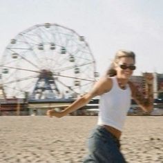 a woman is running on the beach with a ferris wheel in the backgroud