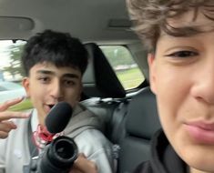 two young men sitting in the back seat of a car, one holding a camera