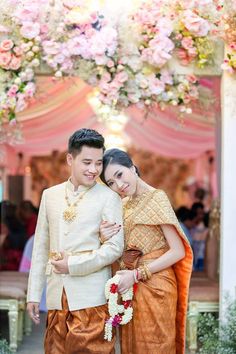 two people standing next to each other in front of a flower covered archway with pink and white flowers