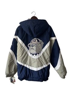 "early 90s georgetown hoyas heavyweight winter coat. deadstock. NWT. navy, white, & grey. zip off hood. metal logo zipper. adjustable drawstring hood. sewn patch logo on back. embroidered chest logo. zip front pockets. 29\" long. 28\" across. 26.5\" sleeves from shoulder seam to cuff. in excellent, unworn condition. legit. legitvintage.etsy.com legitvintage on instagram" Collegiate Winter Track Jacket For Streetwear, Collegiate Style Winter Track Jacket For Streetwear, Collegiate Windbreaker For Winter Streetwear, Collegiate Windbreaker For Streetwear In Winter, Collegiate Hooded Sports Outerwear, Hooded Outerwear For College Sports Season, College Sports Hooded Outerwear, Throwback Outdoor Outerwear For Fall, Navy Fleece-lined Outerwear For Streetwear