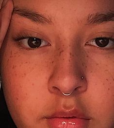 a close up of a person with freckles on their nose and nose piercings