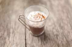 a glass cup filled with hot chocolate on top of a wooden table and topped with whipped cream