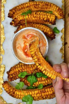 a person is dipping something in a small bowl with corn on the cob next to it