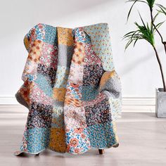 a multicolored blanket sitting on top of a wooden chair next to a potted plant